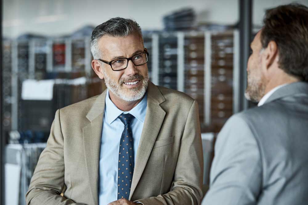 Older man in a suit smiling at another man in a suit