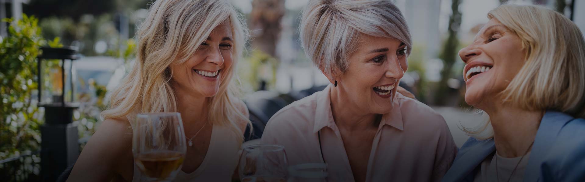 Three older women laughing and smiling at a table with wine